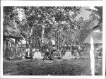 Royal Samoan council sitting on the ground amongst villagers in a Samoan village, ca.1900