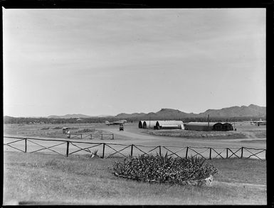 Tontouta Airfield with tin buildings in the foreground and a Dakota transport plane on the runway beyond, New Caledonia