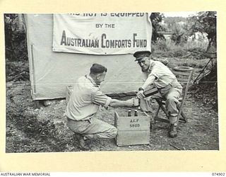 MADANG, NEW GUINEA. 1944-07-20. HONORARY COMMISSIONER H. HEARN, AUSTRALIAN COMFORTS FUND JOKINGLY SERVING A BEER TO ONE OF HIS STAFF AT THE UNIT STORE