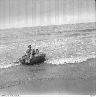 WIRUI BEACH, WEWAK AREA, NEW GUINEA. 1945-08-31. WARRANT OFFICER 2 C. KEAN (1), AND SERGEANT M.C. ARNOLD (2), MEMBERS OF 2/1 FIELD AMBULANCE FLOATING IN THE SURF ON A RUBBER TUBE FROM A JAPANESE ..
