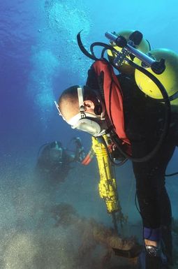 MASTER CHIEF (UCCM) Michael R. Oliver of Underwater Construction Team Two (UCT-2) drills holes in the coral bed next to an underwater cable for clamps to stabilize the cable at the Pacific Missile Range Facility at Kauai, Hawaii