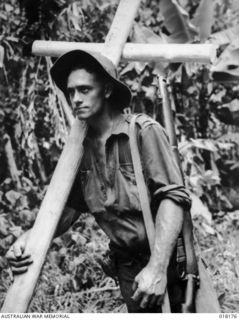 Tsimba area, Bougainville. 27 February 1945. A cross is hewn from rough forest timber to be conveyed by an Australian infantrymen to a forward position to mark the burial place of an Australian ..