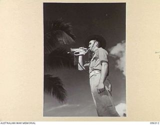 KAHILI, SOUTH BOUGAINVILLE. 1945-09-09. THE BUGLER, SOUNDS REVEILLE AS THE AUSTRALIAN FLAG IS RAISED AT BUIN BY THE BUIN LIAISON GROUP, 2 CORPS