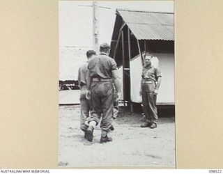 CAPE PUS, NEW GUINEA. 1945-11-03. CHAPLAIN N.D. WINN, 2/2 INFANTRY BATTALION, WAITING AT THE ENTRANCE TO THE CHAPEL TO GREET THOSE WHO ENTER TO PAY HOMAGE TO THEIR FALLEN COMRADES