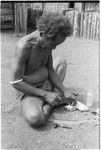 Iika chipping edges off of coneshells with a knife, one step in making kofu shell money beads, at Fanuaba'ita