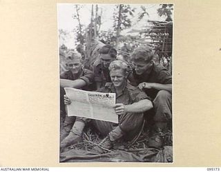 COCONUT KNOLL, KIARIVU, NEW GUINEA, 1945-08-11. MEMBERS OF 2/7 INFANTRY BATTALION READING A COPY OF THE ARMY NEWSPAPER, GUINEA GOLD, DROPPED BY AN ROYAL AUSTRALIAN AIR FORCE AIRCRAFT ON THEIR ..