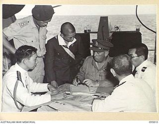 Brigadier W.C.D. Veale, Chief Engineer First Army in conference with Japanese staff officers after the surrender ceremony aboard the aircraft carrier HMS Glory. The surrender of all Japanese forces ..