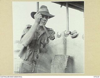 LAE, NEW GUINEA. 1944-08-06. QX19131 LIEUTENANT E.J. BATES, SECTION LEADER 2/3RD FORESTRY UNIT FITTING A NEW TOOTH INTO A LARGE INSERT TOOTH CIRCULAR SAW IN THE UNIT WORKSHOPS