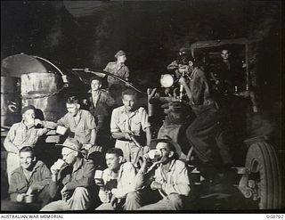 NADZAB, NEW GUINEA. C. 1944-02. PERSONNEL OF NO. 62 MOBILE WORKS SQUADRON RAAF SITTING WITH A DRINK OF TEA ON NIGHT SHIFT WHILE THEIR TRACTOR IS BEING REFUELLED