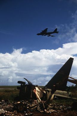 A B-52 aircraft flies over the remains of a B-52D that is destined for the scrap heap in accordance with the SALT II treaty between the United States and the Soviet Union