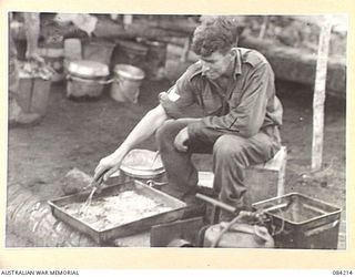SUAIN PLANTATION, NEW GUINEA. 1944-12-08. SERGEANT R.H. HUNTER, A COMPANY, 2/4 INFANTRY BATTALION, PREPARING A DISH OF BULLY BEEF RATIONS DURING A PATROL INTO AN AREA WEST OF THE DANMAP RIVER