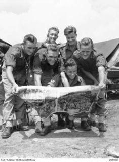 WEWAK POINT, NEW GUINEA. 1945-08-29. SOME MEMBERS OF NO. 8 PLATOON, A COMPANY, 2/8 INFANTRY BATTALION, READING VICTORY NEWS AND VIEWING THE CELEBRATION PICTURES FROM HOME