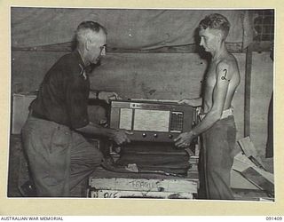 JACQUINOT BAY, NEW BRITAIN, 1945-04-28. CAPTAIN W.E. PARKER, AUSTRALIAN COMFORTS FUND COMMISSIONER (1), AND PRIVATE S.R. KENCHINGTON (2), LIFTING OUT AUSTRALIAN COMFORTS FUND PARCELS. THIS WIRELESS ..