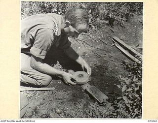 MADANG - ALEXISHAFEN ROAD, NEW GUINEA. 1944-04-27. WX15750 LIEUTENANT J.T. OULD, OFFICER IN CHARGE OF THE PIONEER PLATOON, 30TH INFANTRY BATTALION, LIFTS FROM THE ROAD A JAPANESE LAND MINE BURIED ..