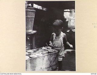 RATONGOR, NEW BRITAIN. 1945-09-19. A SMALL CHINESE BOY EXPECTANTLY HAMMERING AT A BOX OF RED CROSS SUPPLIES AT THE CHINESE INTERNMENT CAMP SOON AFTER THEIR LIBERATION