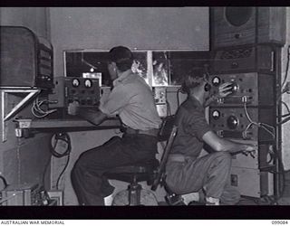 TOROKINA, BOUGAINVILLE, 1945-11-26. SIGNALMAN R. ASHTON (1) AND LANCE-CORPORAL J. BURRELL (2), OPERATORS AT THE BOARD IN THE CONTROL ROOM OF RADIO STATION 9AC TOROKINA, AUSTRALIAN ARMY AMENITIES ..