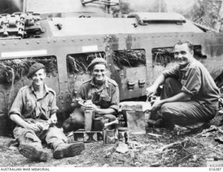 Huon Peninsula, New Guinea. 1943-12. A tank crew of No. 1 Australian Tank Battalion 2nd AIF pause for a meal while pursuing Japanese in flight from Gusika, a coastal village. Left to right Trooper ..