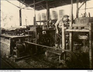 Lae, New Guinea. 1944-07-26. Two Chevrolet motor engines used to supplement power at the 2/3rd Forestry Company sawmill in the Busu Forest. The fitter is shown making an adjustment