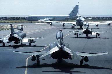 Two KC-135 Stratotanker aircraft taxi onto the runway as three 563rd Tactical Wing F-4G Wild Weasel Phantom II aircraft stand by on the flight line during Exercise Team Spirit '85
