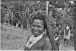 Smiling woman with beaded necklace and shell valuable, carries netbag slung from her head