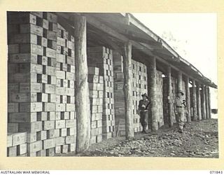 LAE, NEW GUINEA. 1944-03-29. QX6210 CAPTAIN L. B. SCHUBERT (LEFT), WITH QX59038 CAPTAIN J. E. T. WHARTON (RIGHT), MEMBERS OF THE 39TH SUPPLY DEPOT COMPANY, ALONGSIDE BULK STORES OF 40,000 CASES OF ..