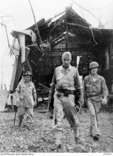 1943-01-14. ONE OF THE BULLET RIDDLED BUILDINGS AT BUNA MISSION, THE SCENE OF SOME OF THE FIERCEST FIGHTING OF THE PAPUAN CAMPAIGN. IN THE FOREGROUND IS GENERAL SIR THOMAS BLAMEY AND LIEUT GENERAL ..