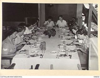 LAE, NEW GUINEA. 1945-11-08. AUSTRALIAN WOMEN'S ARMY SERVICE STUDENTS WITH THEIR TWO INSTRUCTORS (AT END OF TABLE) EATING THE MEAL THEY HAVE PREPARED DURING THE COOKERY AND HOME CRAFT COURSE HELD ..
