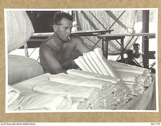 17 MILE, PORT MORESBY AREA, NEW GUINEA. 1943-12-04. WX5515 CORPORAL F. SMITH OF THE 9TH AUSTRALIAN DIVISION MOBILE LAUNDRY PREPARING QUANTITIES OF SHEETS FOR DESPATCH TO HOSPITALS IN THE AREA