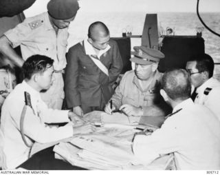 Brigadier W.C.D. Veale, Chief Engineer First Army in conference with Japanese staff officers after the surrender ceremony aboard the aircraft carrier HMS Glory. The surrender of all Japanese forces ..