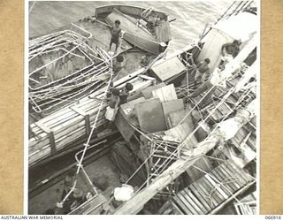 MILNE BAY, NEW GUINEA, AUSTRALIA. 1944-06-14/02. THE AK94 A VESSEL OF THE 12TH SMALL SHIPS COMPANY, TAKING LANDING BARGE STANCHIONS ABOARD AS SHE STANDS OFF KWIARI