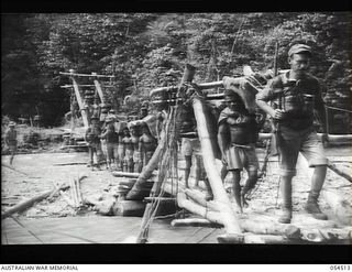 Mubo-Salamaua, New Guinea. 1943-07-21. Private First Class L. Simon, United States Army, of Los Angeles with the Allied Supply Corps, leading a food line of native bearers across the Bitoi River ..