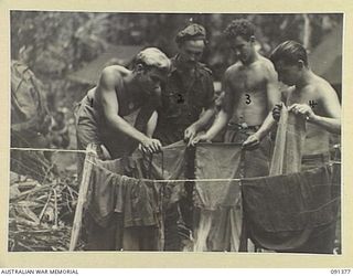 BOUGAINVILLE. 1945-04-30. TROOPS OF 9 INFANTRY BATTALION DRYING THEIR CLOTHES WITH THE AID OF A FIRE BECAUSE OF THE CONTINUAL RAIN. IDENTIFIED PERSONNEL ARE:- PRIVATE G.I. STEWART (1); SERGEANT E. ..