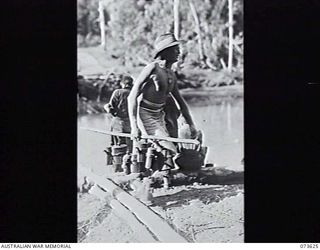 MARUKINAM RIVER, NEW GUINEA. 1944-05-28. N205084 PRIVATE F. A. ROBINSON, 35TH INFANTRY BATTALION, CARRIES WATER FROM THE RIVER IN WATER BOTTLES STRUNG ON A LONG STICK. THE UNIT IS CAMPED AT THE ..