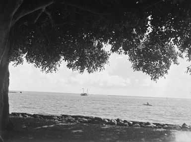 [View of a small boat at sea as seen from a stone-lined beach]