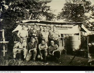 Lae, New Guinea. c. 1944-04. Informal group portrait of members of No 1 Section, Detached, 2 Field Survey Company, off duty at Main Camp, Butibum Road. Note improvised gutter and 44 gallon drum to ..