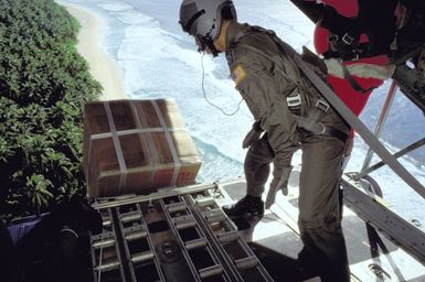 Personnel from the 345th and 21st Tactical Airlift Squadrons release a package out of the cargo bay of a C-130 Hercules aircraft. Donated Christmas gifts are being parachuted onto local islands