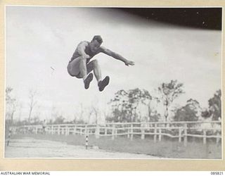 HERBERTON, QLD. 1945-01-19. GUNNER H M EQUID, 2/12 FIELD REGIMENT, JUMPING 20 FEET 1 1/2 INCHES IN THE BROAD JUMP EVENT DURING THE 9 DIVISION GYMKHANA AND RACE MEETING HELD AT HERBERTON RACECOURSE