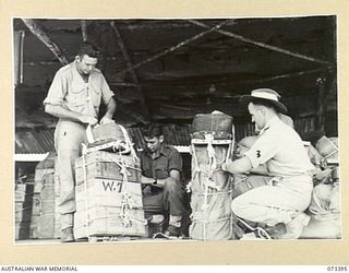 NADZAB, NEW GUINEA. 1944-05-25. MEMBERS OF THE 3RD AIR MAINTENANCE COMPANY FITTING AN AMERICAN PARACHUTE TO A PACK (ON THE LEFT), DESIGNED TO FIT A DOUGLAS AIRCRAFT. AT THE RIGHT A "POL" (PETROL, ..