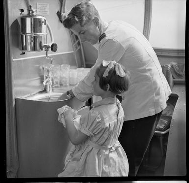 Young child Jennifer Gray, a passenger on Qantas Catalina flying boat service from Suva, Fiji, to Sydney, Australia, helping steward R M White with dishes