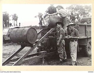 LAE AREA, NEW GUINEA. 1945-07-12. MEMBERS OF 2 BULK PETROLEUM STORAGE COMPANY, USING MECHANICAL DRUM SKIDS TO LOAD 44-GALLON DRUMS OF MOTOR SPIRIT