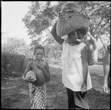 Woman carrying a bag on her head and with a child walking to the Boong, native markets, Rabaul, New Guinea, ca. 1936 / Sarah Chinnery