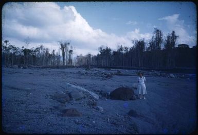 Sister Gilbert at the Andemba River, standing by a large, hot rock deposited by the volcano overnight, Papua New Guinea, 1951 / Albert Speer