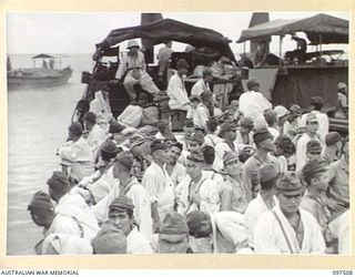 FAURO ISLAND, BOUGAINVILLE AREA. 1945-10-01. JAPANESE TROOPS, WITH PATIENTS FOR ADMISSION TO HOSPITAL WEARING WHITE COATS WITH RED CROSS ATTACHED, STANDING IN A BARGE WAITING FOR THE ORDER TO MOVE ..