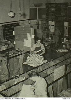 North Qld. C. 1943-10. Warrant Officer J. Dwan of East Brisbane, Qld, furthest from camera, and Aircraftman 1 P. W. Kirkpatrick of Cessnock, NSW, sorting newspapers into bags at a RAAF post office ..