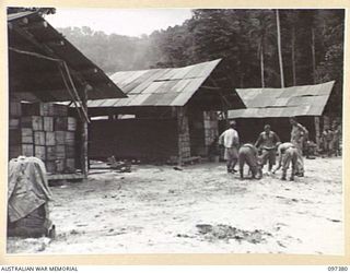 FAURO ISLAND, BOUGAINVILLE AREA. 1945-09-29. JAPANESE RATIONS STACKED ALONGSIDE AUSTRALIAN RATIONS FOR USE ON FAURO ISLAND. JAPANESE TROOPS AT WORK IN FOREGROUND CLEARING THE AREA. THE SURRENDER ..