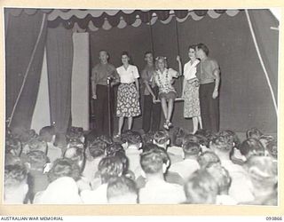 LAE AREA, NEW GUINEA, 1945-07-09. SIGNALWOMAN J.D. HUNT (1), ON A SWING PLAYING THE PART OF "MARGIE" THE MAIN CHARACTER IN "A PRETTY GIRL" PRESENTED DURING THE REVUE "OVER TO YOU". IT WAS STAGED BY ..