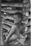 Boy leans against wall of a yam house, with good detail of notched pole construction