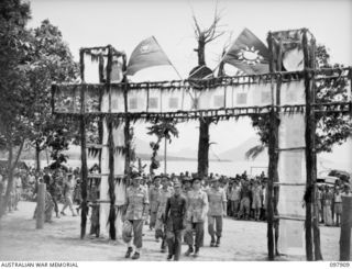 RABAUL, NEW BRITAIN. 1945-10-10. MAJOR GENERAL K.W. EATHER, GENERAL OFFICER COMMANDING 11 DIVISION, ACCOMPANIED BY COLONEL WOO YIEN AND OFFICIAL PARTY, PASSING THROUGH AN ARCHWAY DURING INSPECTION ..
