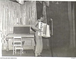 LAE AREA, NEW GUINEA. 1945-01-28. NX157626 CORPORAL R. RUDGLEY, PIANO ACCORDIONIST, OF THE "TANKS A MILLION CONCERT PARTY" PLAYING THE "THE TWELFTH STREET RAG" DURING A CONCERT STAGED BY THE DICK ..