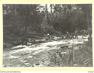 GENARA RIVER, NEW GUINEA. 1944-04-15. MEMBERS OF THE 24TH LINE SECTION, 18TH LINES OF COMMUNICATION SIGNALS CROSSING A SUSPENSION BRIDGE OVER THE GENARA RIVER ACCOMPANIED BY NATIVE CARRIERS